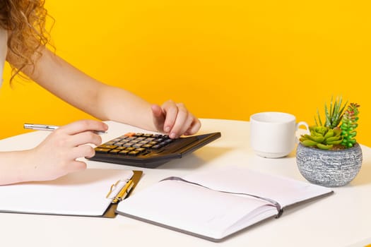 A young woman sits at a table, works with documents, considers, studies. Education. Business. Isolated on yellow background