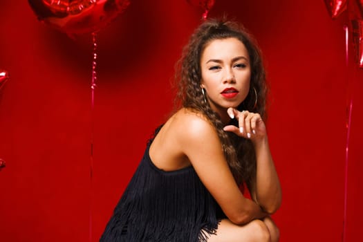 Funny girl with red balloons on a red background. Young woman festive mood with balloons in the form of numbers and stars.