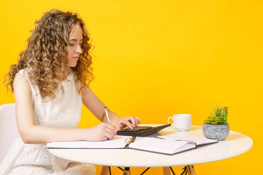 A young woman sits at a table, works with documents, considers, studies. Education. Business. Isolated on yellow background