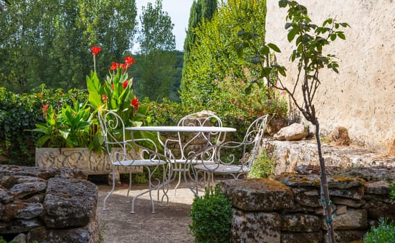 a cozy patio with metal white chairs and table between the blooming flowers and plants in france