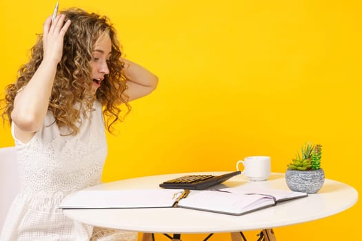 A young woman sits at a table, works with documents, considers, studies. Education. Business. Isolated on yellow background