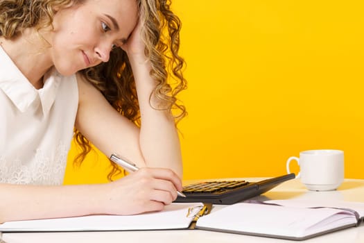 A young woman sits at a table, works with documents, considers, studies. Education. Business. Isolated on yellow background