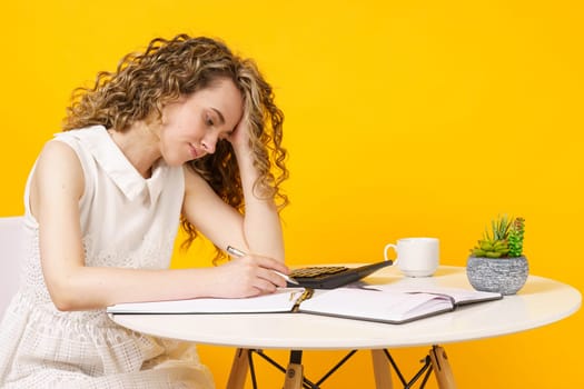 A young woman sits at a table, works with documents, considers, studies. Education. Business. Isolated on yellow background