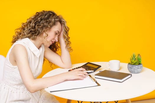 A young woman sits at a table, works with documents, considers, studies. Education. Business. Isolated on yellow background