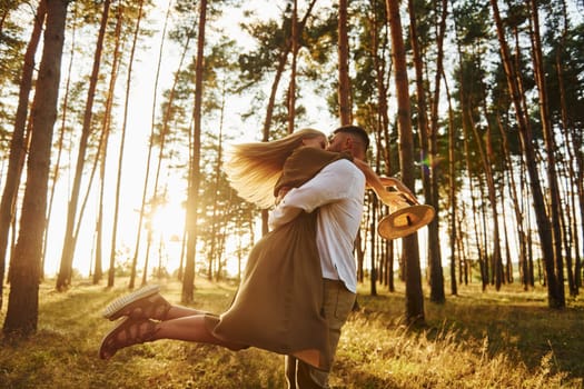 Against background with sunshine. Happy couple is outdoors in the forest at daytime.