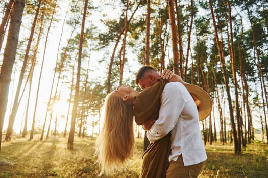 Against background with sunshine. Happy couple is outdoors in the forest at daytime.