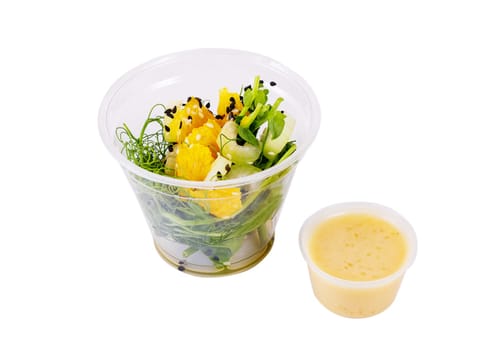 Salad with microgreens peas, spinach, celery, orange, sesame seeds and dressing in plastic cup on white background