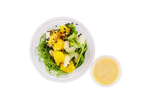 Salad with microgreens peas, spinach, celery, orange, sesame seeds and dressing in plastic cup on white background