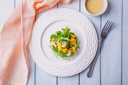 Salad with microgreens of peas, spinach, celery, orange, sesame seeds and dressing in plate on white wooden background