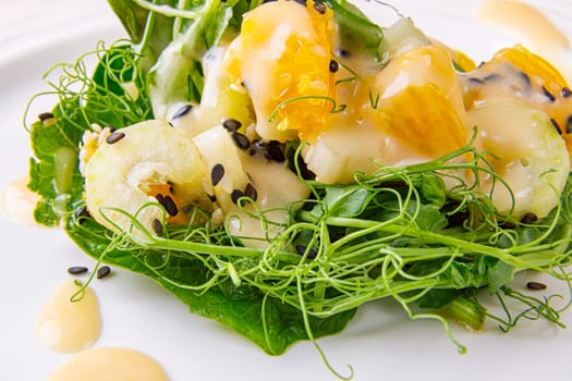 Salad with microgreens of peas, spinach, celery, orange, sesame seeds and dressing in plate on white wooden background