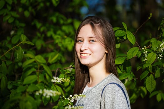 Portrait of a girl on a background of green foliage. Beautiful young woman of caucasian ethnicity smiling on a sunny spring day