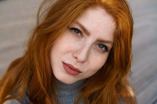 female closeup portrait, caucasian red-haired cute young woman with freckles and green eyes looks into the frame and cute smiling