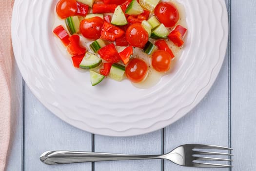 Salad of cucumbers, cherry tomatoes, peppers and dressing in a plate on a white wooden background