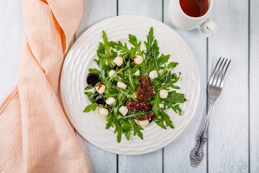 Fresh salad with arugula, mozzarella cheese, sun-dried tomato and white wood dressing