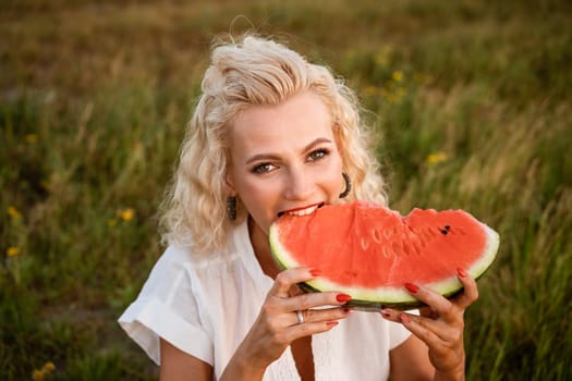 Close-up portrait of a woman biting a watermelon in nature. Beautiful girl of caucasian appearance eats a watermelon on a picnic.
