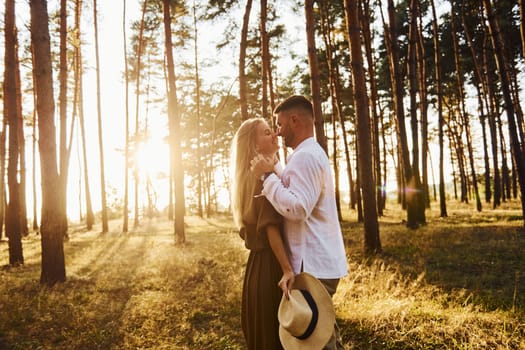 Man is in white shirt and woman in dress. Happy couple is outdoors in the forest at daytime.