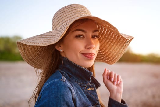 Young woman in a hat against the blue sea. Portrait of a young attractive girl in a straw hat on the beach in the evening at sunset, close up