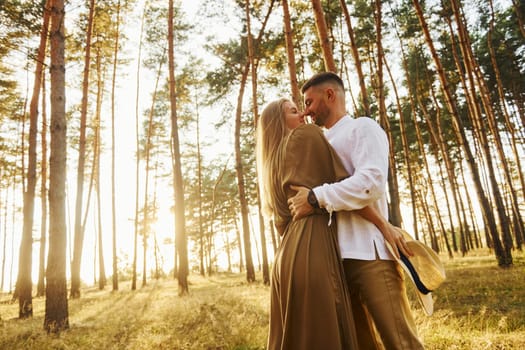 Man is in white shirt and woman in dress. Happy couple is outdoors in the forest at daytime.