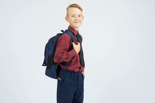 A schoolboy holds a school backpack, stands sideways, looks at the camera. Education concept