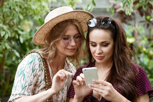 Two beautiful women friends in the park looking at the phone.