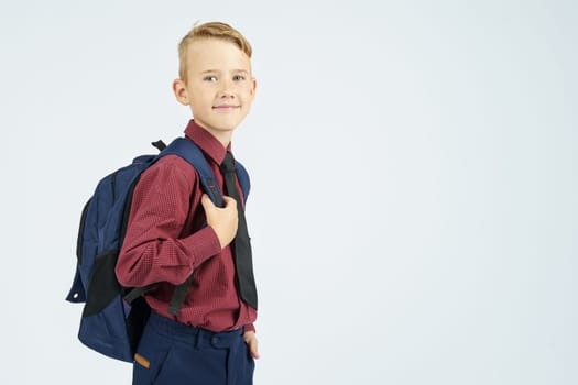 A schoolboy holds a school backpack, stands sideways, looks at the camera. Education concept