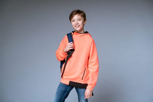 a guy teenager of European appearance in a bright orange sweater posing with a backpack on a gray background, a happy young guy smiling with a white smile