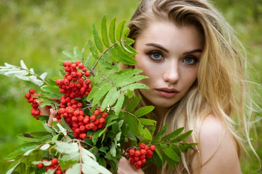 Portrait of a young beautiful blonde woman with a bouquet of rowan berries in nature close-up