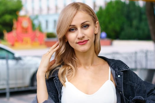 Portrait of a blonde woman on a city street. Young beautiful woman of Caucasian ethnicity in a white tracksuit posing in the city.