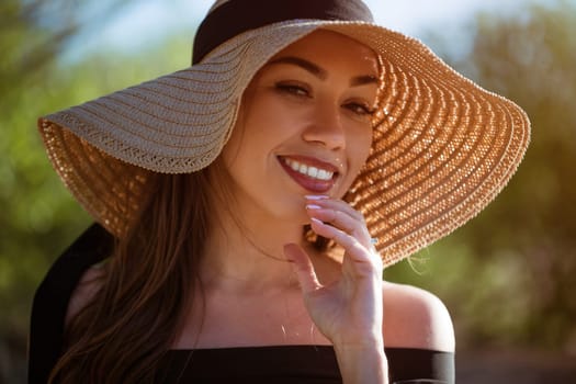 Beautiful young woman in a straw hat in black outdoors on a sunny day smiling, close-up. Happy caucasian girl in the summer on nature