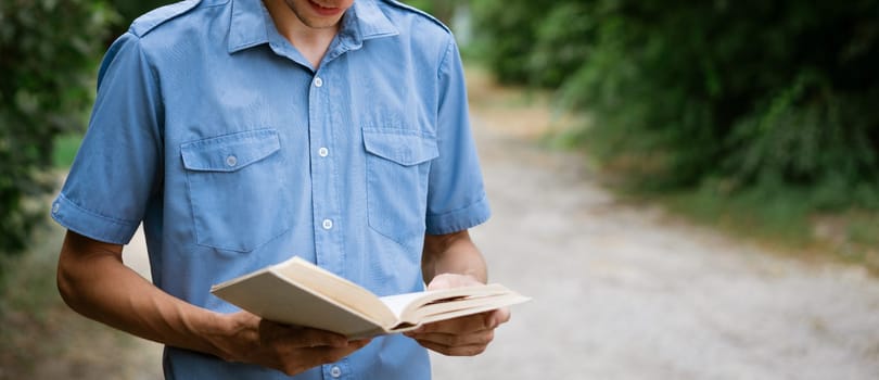 Student guy in a blue shirt with a book in his hand in the park reads