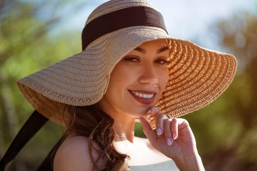 Cheerful young woman in straw sun hat smiles toothy smile close up on summer sunny day