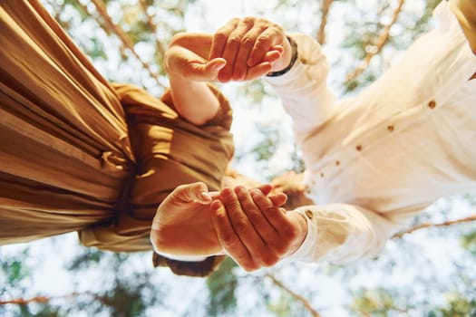 View from below. Happy couple is outdoors in the forest at daytime.