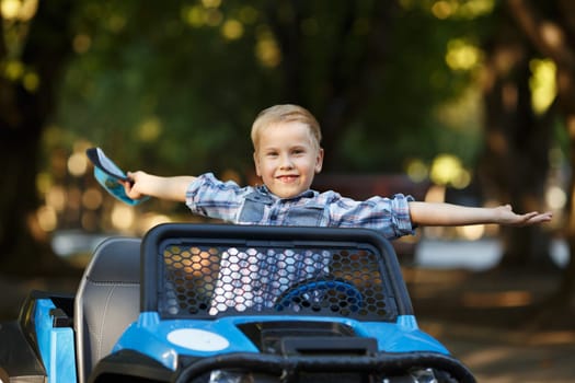 The boy plays, drives a car in the park. A cute little boy of Caucasian appearance in a cap driving a large mechanical toy truck,