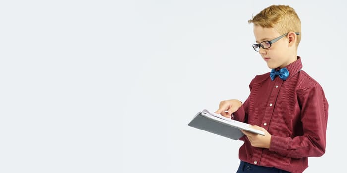 A schoolboy with glasses reads a book he holds in his hands. Isolated background. Education concept