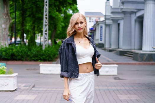 Portrait of a blonde woman on a city street. Young beautiful woman of Caucasian ethnicity in a white tracksuit posing in the city.