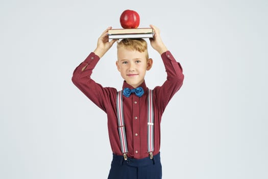 A schoolboy holds books with an apple on his head, smiles. Isolated background. Education concept