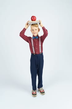 A schoolboy holds books with an apple on his head, smiles. Isolated background. Education concept