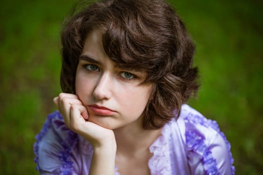 Rubs young sad woman on natural background. Cute girl looks into the camera with green eyes. Caucasian beautiful woman