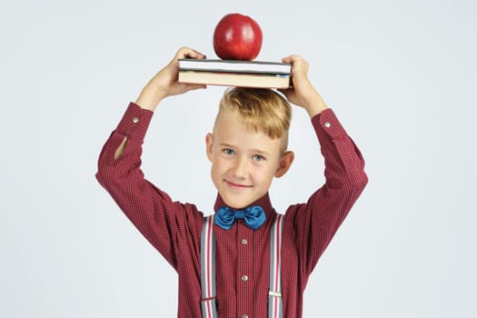 A schoolboy holds books with an apple on his head, smiles. Isolated background. Education concept