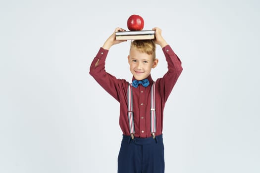 A schoolboy holds books with an apple on his head, smiles. Isolated background. Education concept