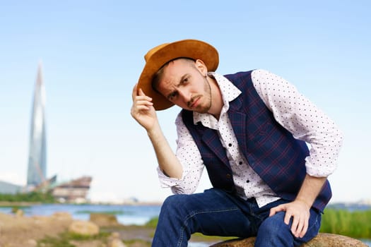 Close up portrait of handsome stylish casual man traveler in hat sitting at sea coastline and enjoying peaceful nature. Close-Up Of Man Wearing Hat Against Sky.