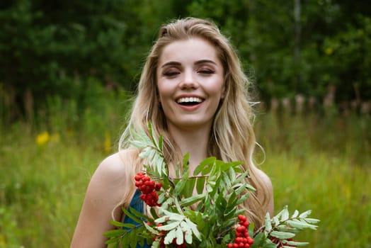 Portrait of a young beautiful blonde woman with a bouquet of rowan berries in nature close-up