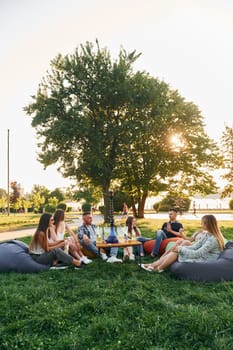 Talking with each other. Group of young people have a party in the park at summer daytime.