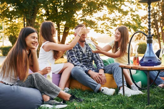 Drinking game. Group of young people have a party in the park at summer daytime.