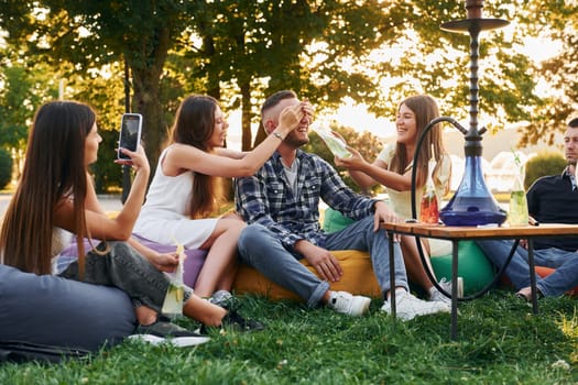 Drinking game. Group of young people have a party in the park at summer daytime.