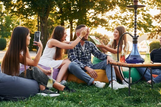 Drinking game. Group of young people have a party in the park at summer daytime.