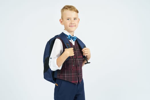 A schoolboy holds a school backpack, stands sideways, looks at the camera. Education concept