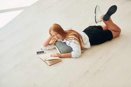 Reading book. Female teenager with blonde hair is at home at daytime.