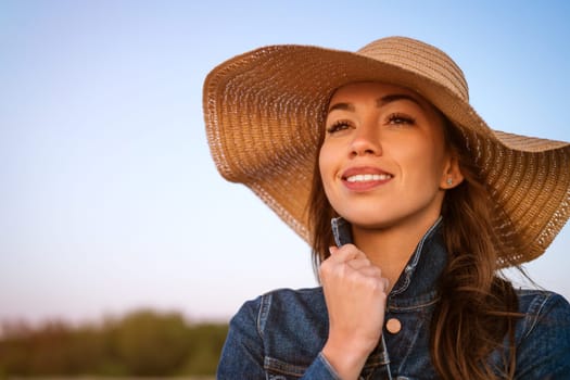 Young woman in a hat against the blue sea. Portrait of a young attractive girl in a straw hat on the beach in the evening at sunset, close up