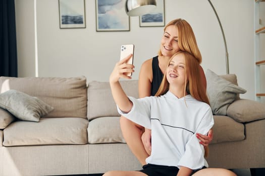 Sitting on the floor. Female teenager with her mother is at home at daytime.